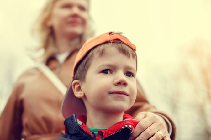 Boy in a cap, with a woman behind holding his shoulder