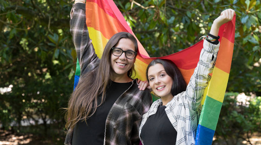Two people holding a Pride flag together behind them